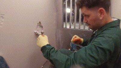a man in a green jacket and yellow gloves is cleaning a wall in a prison cell .
