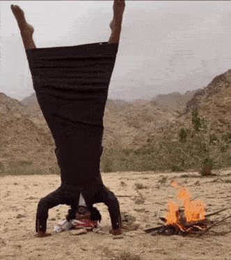 a man is doing a handstand in the desert near a fire