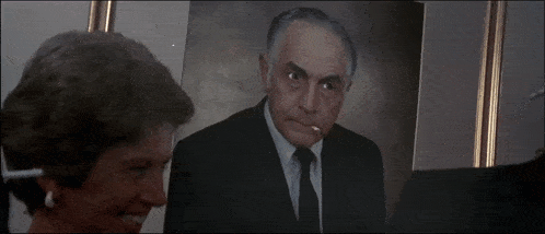 a man in a suit and tie is smoking a cigarette in front of a picture of himself
