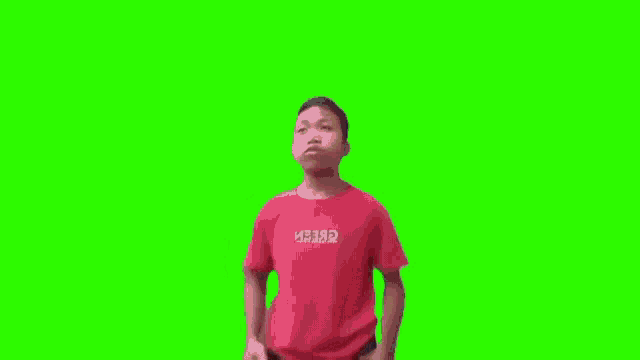 a young boy in a red t-shirt is dancing on a green screen .