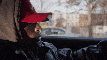 a man wearing a hooded jacket and a red hat looks out the window of a car