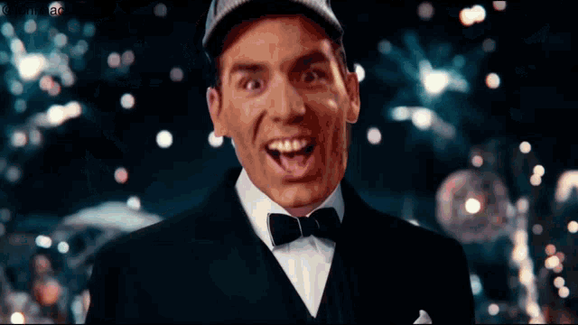 a man in a tuxedo and bow tie is smiling in front of a blurred background
