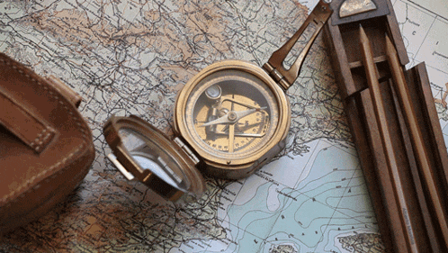 a compass sits on top of a map next to pencils and a leather case