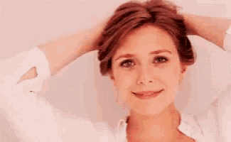 a woman in a white shirt is smiling and holding her hair .