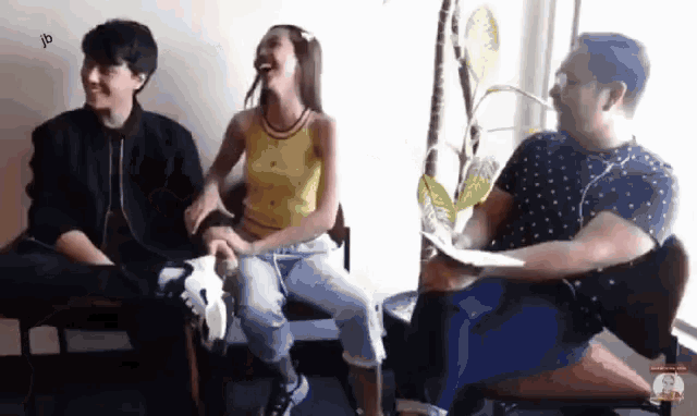 a group of people are sitting in chairs laughing and one of them is wearing a yellow tank top