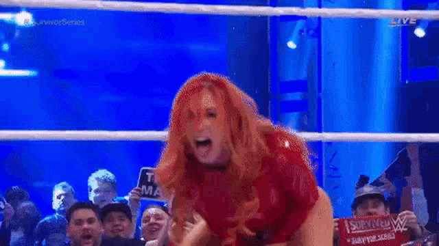 a woman in a red bodysuit is standing in a wrestling ring with her mouth open .