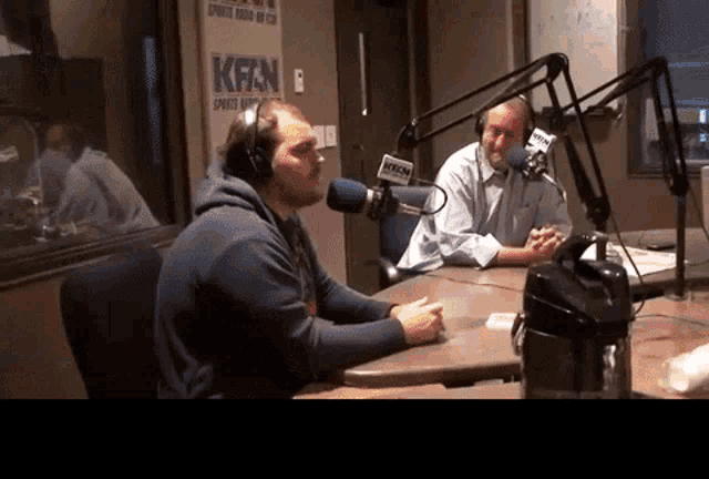 two men are sitting in front of microphones in front of a sign that says kfan