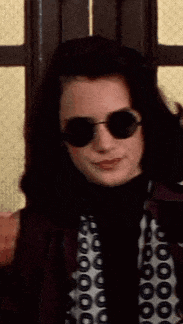 a woman wearing round sunglasses and a polka dot shirt is smiling .
