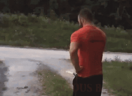 a man in a red shirt is urinating on the side of a road .