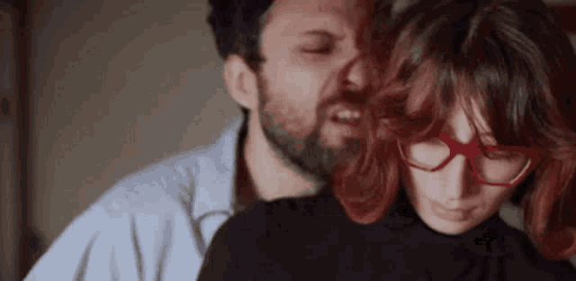 a man with a beard is kissing a woman who is wearing glasses .