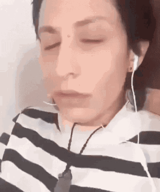 a woman wearing headphones and a striped shirt is laying down with her eyes closed and a nose piercing .