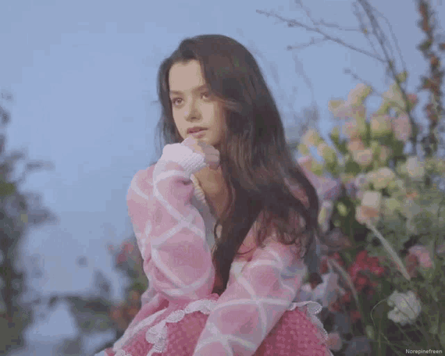 a woman in a pink sweater is standing in front of a bunch of flowers .