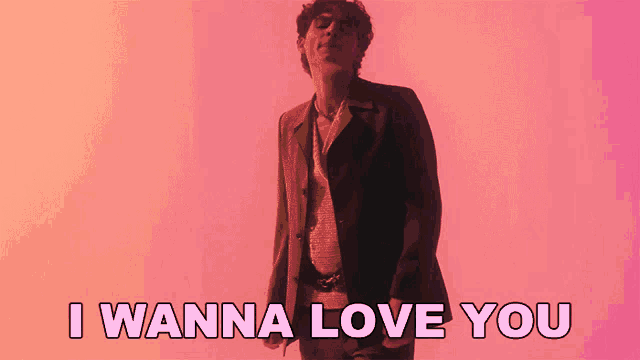a man in a suit is standing in front of a pink background and says i wanna love you