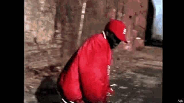 a man wearing a red jacket and a red hat is kneeling down on the ground .