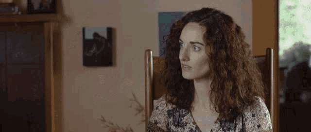 a woman with curly hair sits in a chair in front of a painting