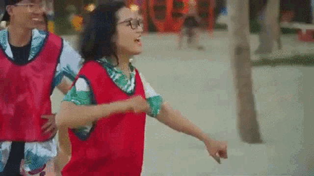 a woman wearing glasses and a red vest is running with a man .
