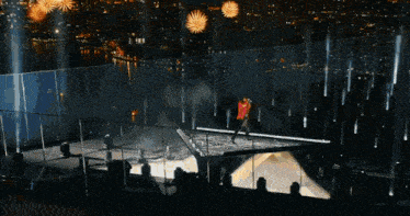 a woman in a red shirt is walking on a stage with fireworks in the background