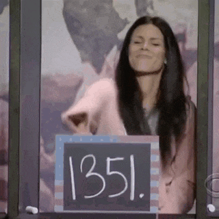 a woman is standing in front of a chalkboard with the number 1351 written on it .