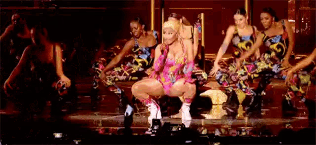 a woman is kneeling down on a stage with a group of dancers .