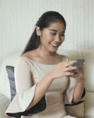 a woman in a white dress is sitting on a couch looking at her cell phone .