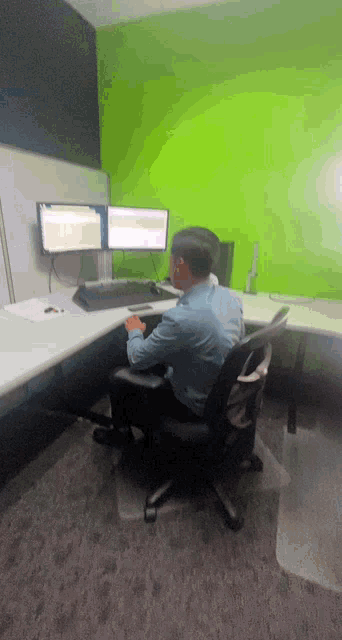 a man sits at a desk with two computer monitors on it