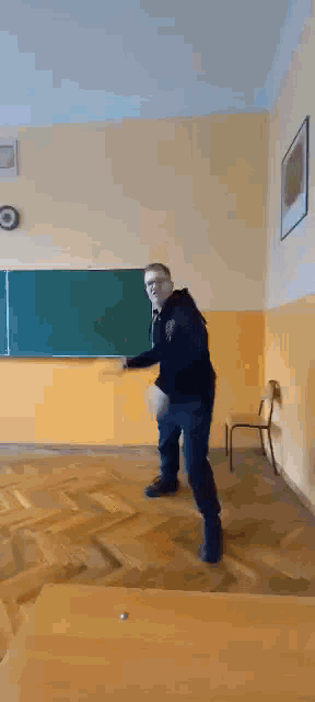 a man is standing in front of a blackboard in a classroom and dancing .