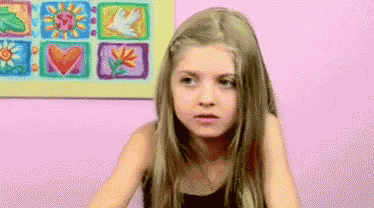 a young girl with long blonde hair is sitting in front of a pink wall with a picture of flowers on it .