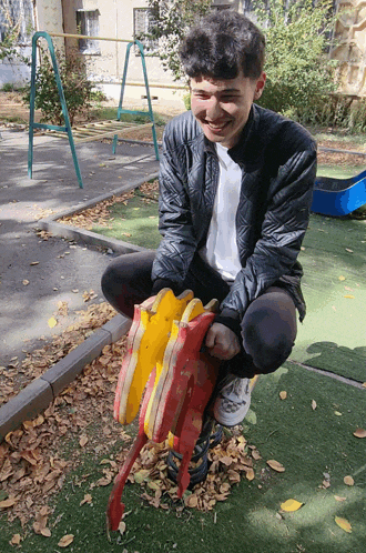 a young man sits on a rocking horse with leaves on it