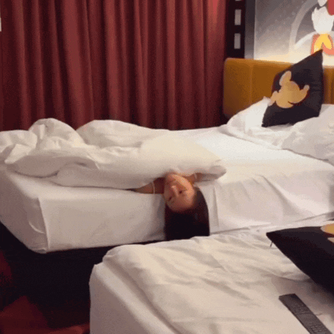 a woman laying on a bed with a mickey mouse pillow on the headboard