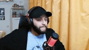 a man with a beard is wearing headphones and a hat and talking into a microphone .