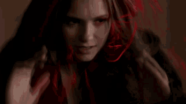 a woman with red eyes is wearing a red hood and looking at the camera .