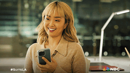 a woman is smiling while holding a cell phone with #suitsla written on the bottom