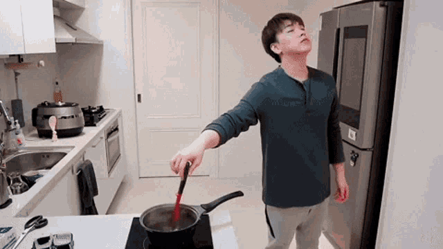 a man in a kitchen is stirring a pot of food with a red spoon