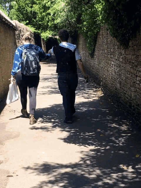 two people walking down a path with a brick wall behind them