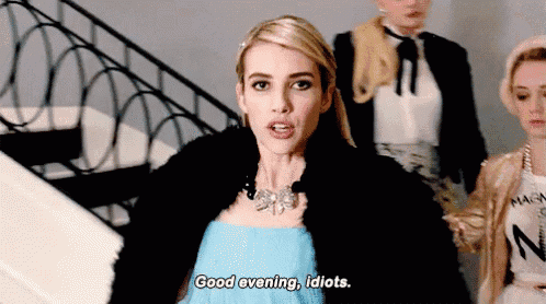 a woman in a blue dress is standing on a set of stairs and says `` good evening , idiots '' .