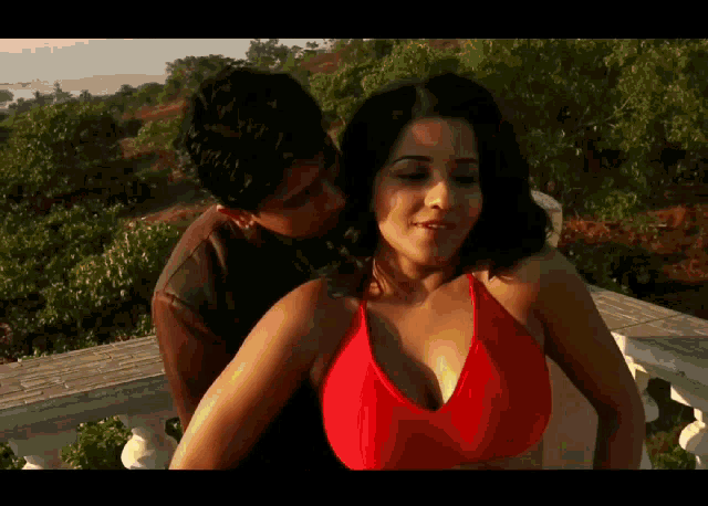 a woman in a red top is being kissed by a man