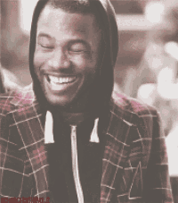 a man wearing a plaid jacket with a hood smiles