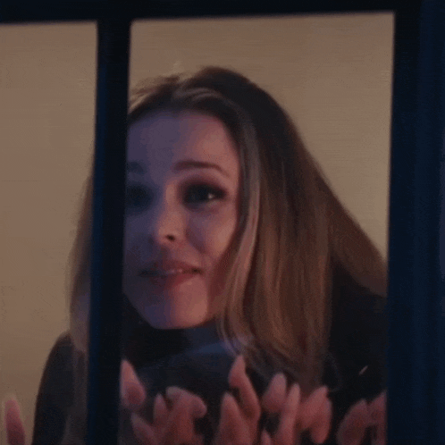 a woman is looking out a window with her hands up