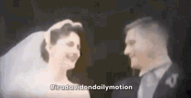 a bride and groom are standing next to each other and looking at each other in a blurry photo .