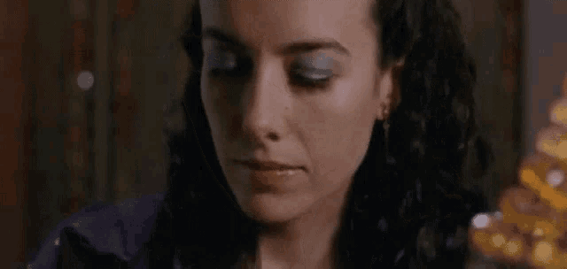 a close up of a woman 's face with a purple shirt and blue eye shadow .