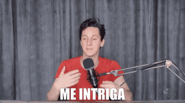 a man in a red shirt speaking into a microphone with the words me intriga behind him