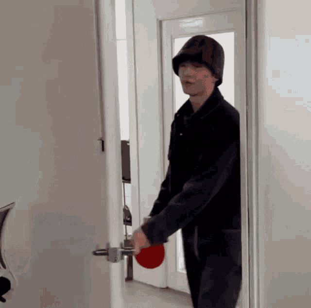 a man in a black hat is holding a red ping pong paddle in his hand while standing in a doorway .