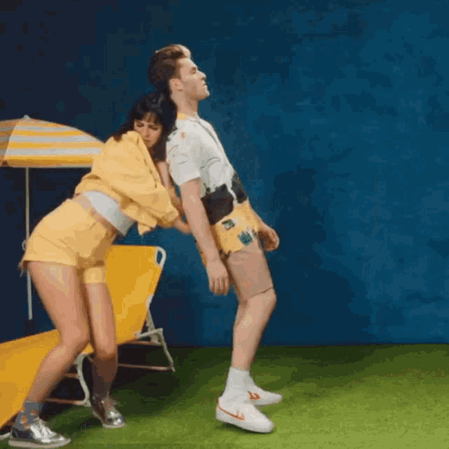 a man and a woman are dancing in front of a beach chair and umbrella