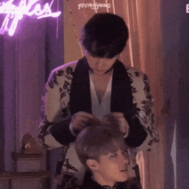 a man is tying another man 's hair while standing next to him .
