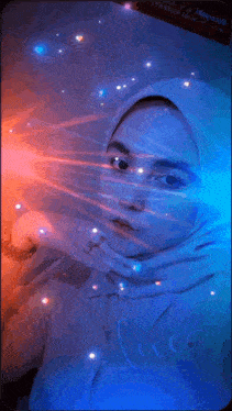 a woman wearing a hijab stands in front of a blue light