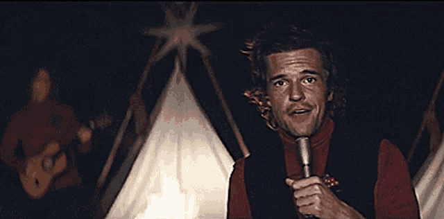 a man singing into a microphone while another man plays a guitar in the background