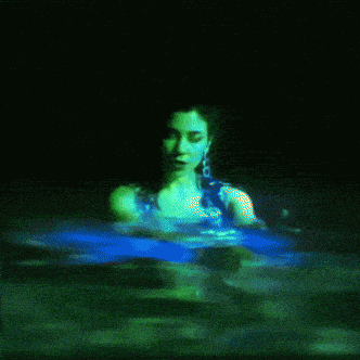 a woman is swimming in a pool with green lights projected on her face