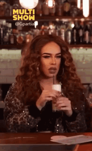 a woman is sitting at a bar holding a drink with a straw and the words multi show behind her