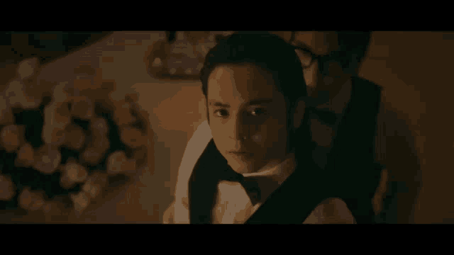 a man in a tuxedo is standing in front of a table with flowers on it