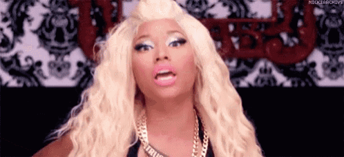 a woman with blonde hair and pink lips is wearing a gold necklace and a black top .